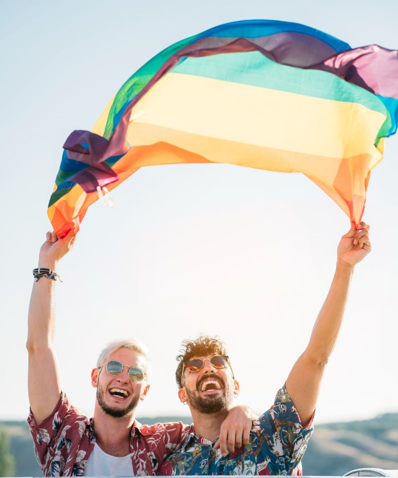 gay-couple-in-van-holding-lgbt-flag-portrait
